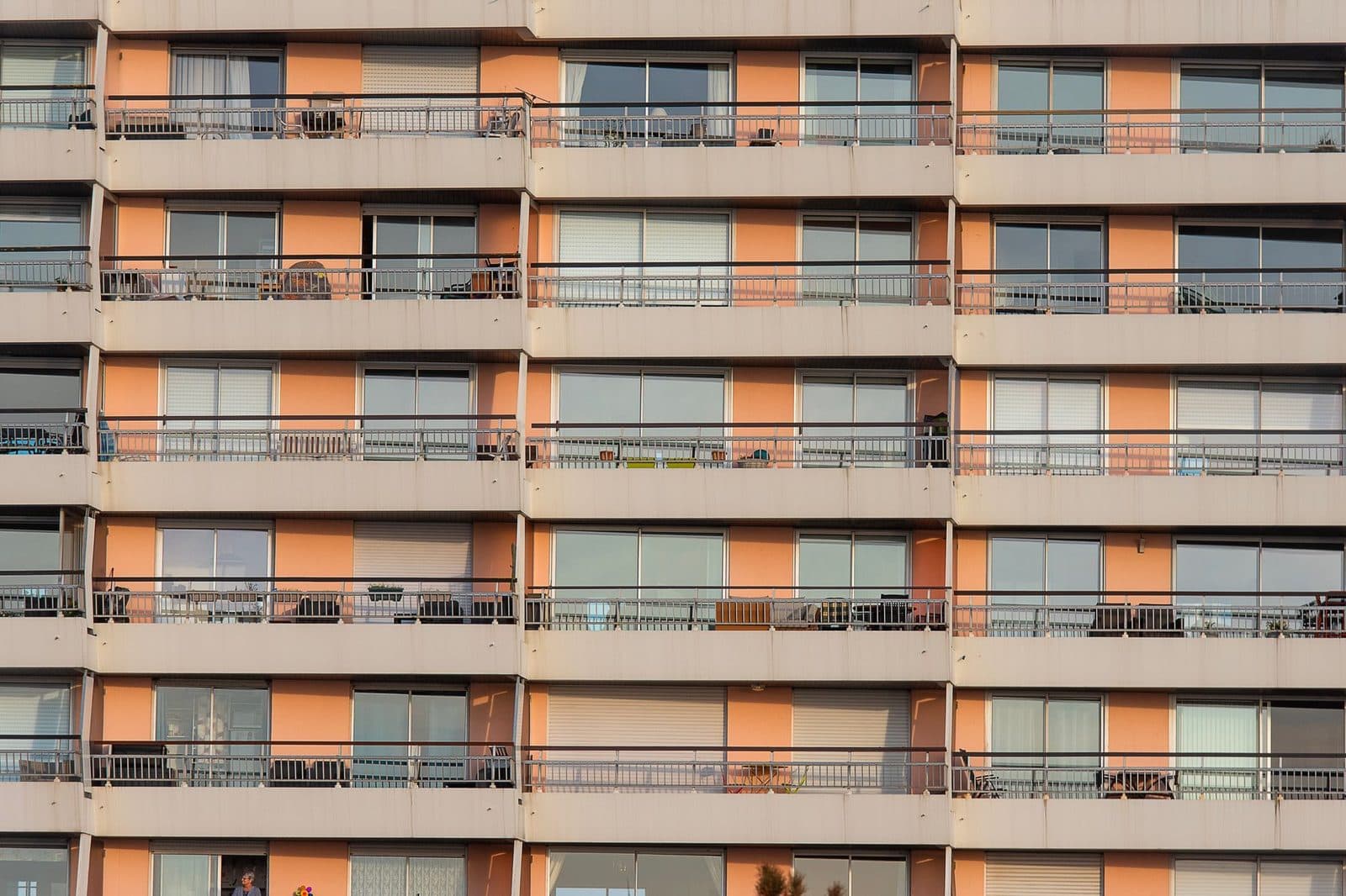 Façade d'un immeuble d'habitation avec balcons alignés et volets orange au coucher du soleil