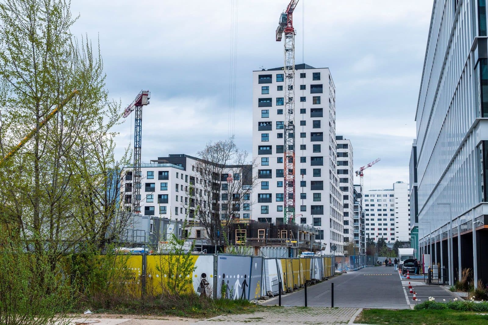 Chantier de construction urbain avec grues, immeubles neufs et palissades le long d'une rue