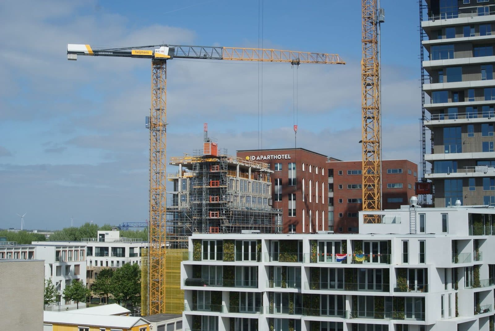 Chantier de construction avec deux grues, immeuble en échafaudage et bâtiments résidentiels modernes