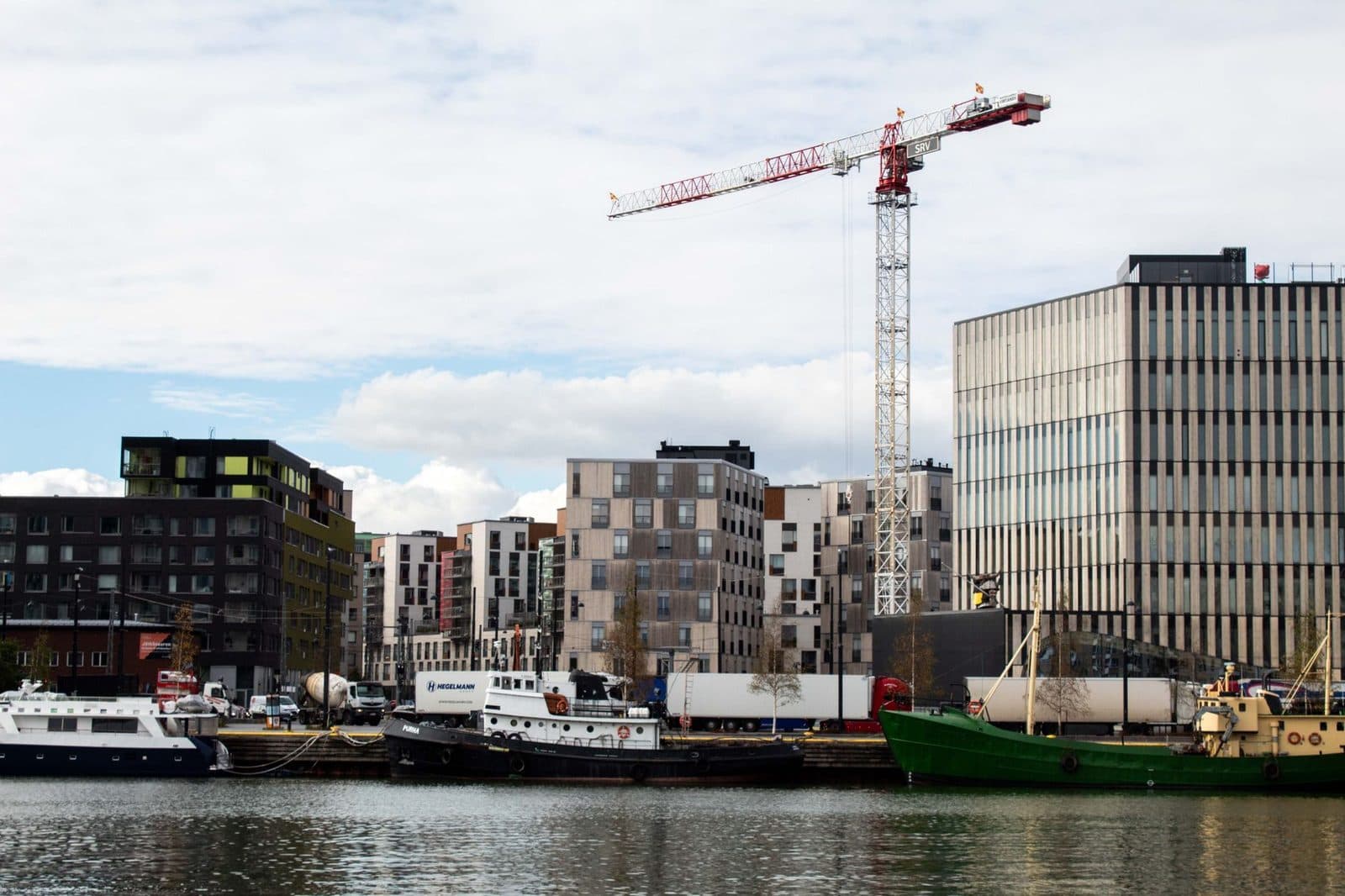 Chantier de construction en bord de quai : grue, immeubles neufs, camion toupie et bateaux amarrés