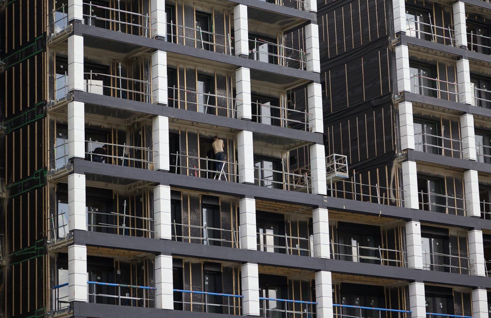 Façade d'un immeuble en construction avec balcons et ouvriers travaillant sur un chantier