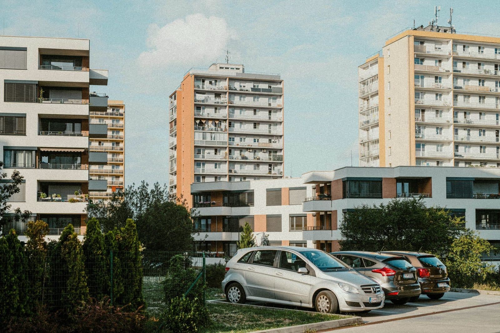 Immeubles d'habitation modernes avec balcons, haie et voitures garées sur un parking en bord de résidence