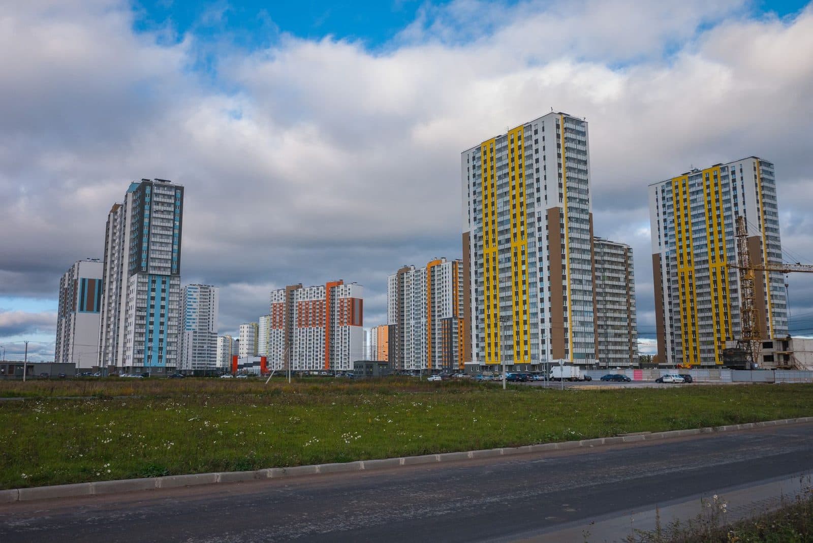 Tours d'habitation neuves aux façades colorées et grue de chantier, terrain vague et route au premier plan