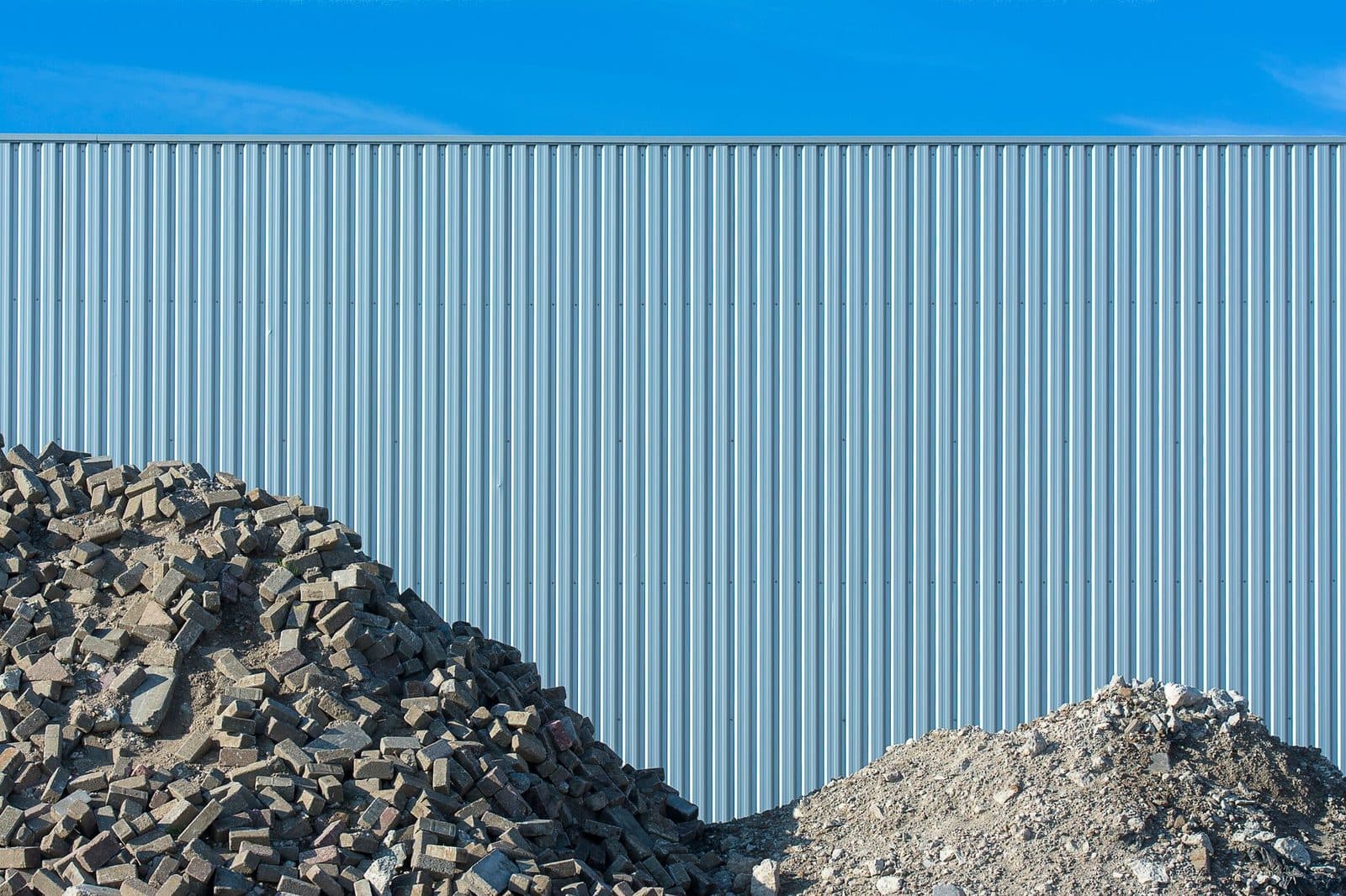 Tas de pavés et gravats de démolition devant une palissade métallique de chantier sous un ciel bleu
