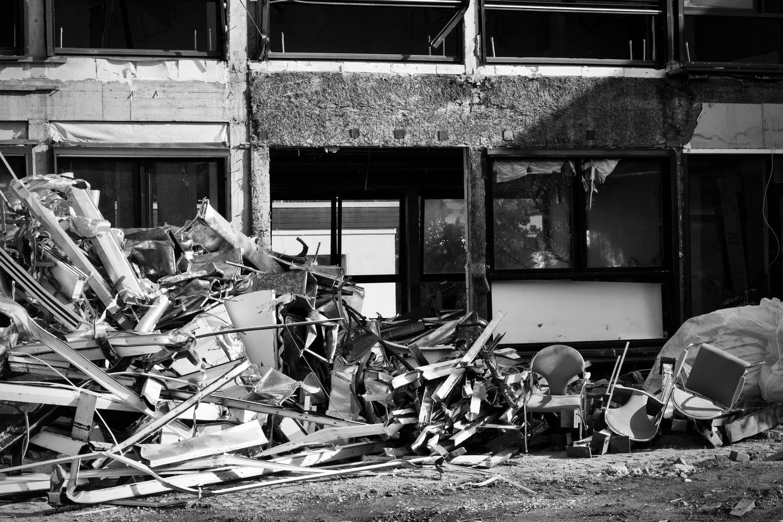 Tas de gravats et de débris métalliques devant un bâtiment en cours de démolition, photo en noir et blanc