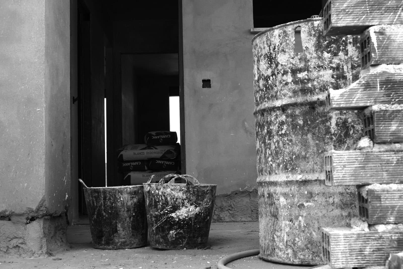 Chantier de construction : bidon, auges de maçon, sacs de ciment et briques devant un mur brut