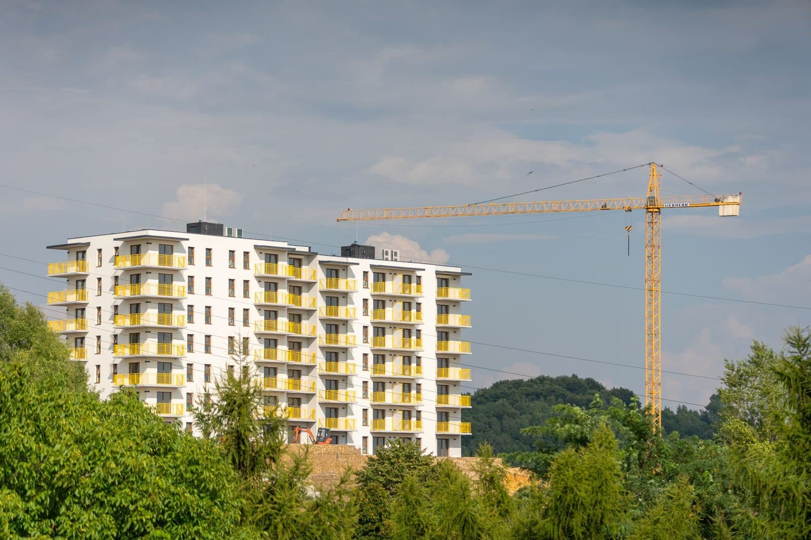 Immeuble de logements neuf aux balcons jaunes en construction, avec une grue jaune, entouré d'arbres