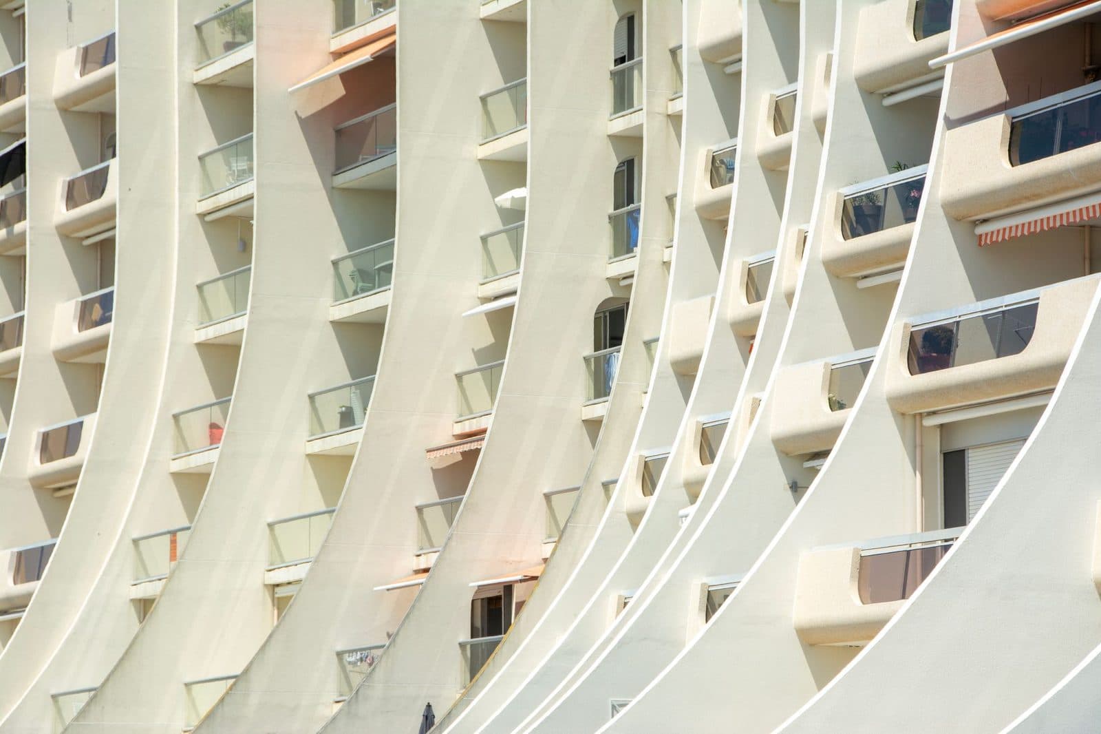 Façade d'un immeuble résidentiel moderne aux lignes courbes, avec balcons vitrés et stores