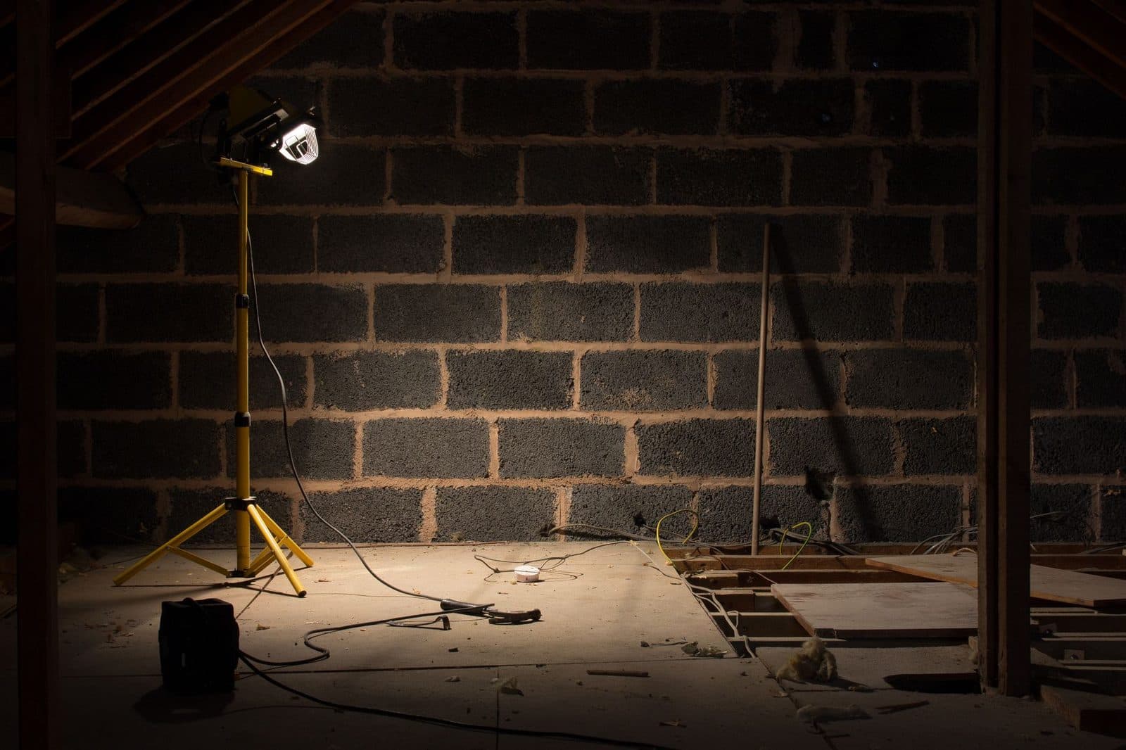 Combles en chantier éclairés par un projecteur de travail, mur en parpaings et plancher en cours de pose