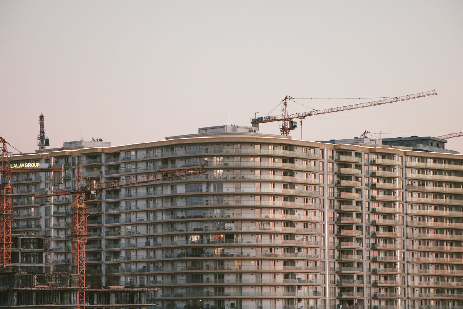 Immeubles résidentiels en construction avec grues de chantier au-dessus des façades à balcons, au crépuscule