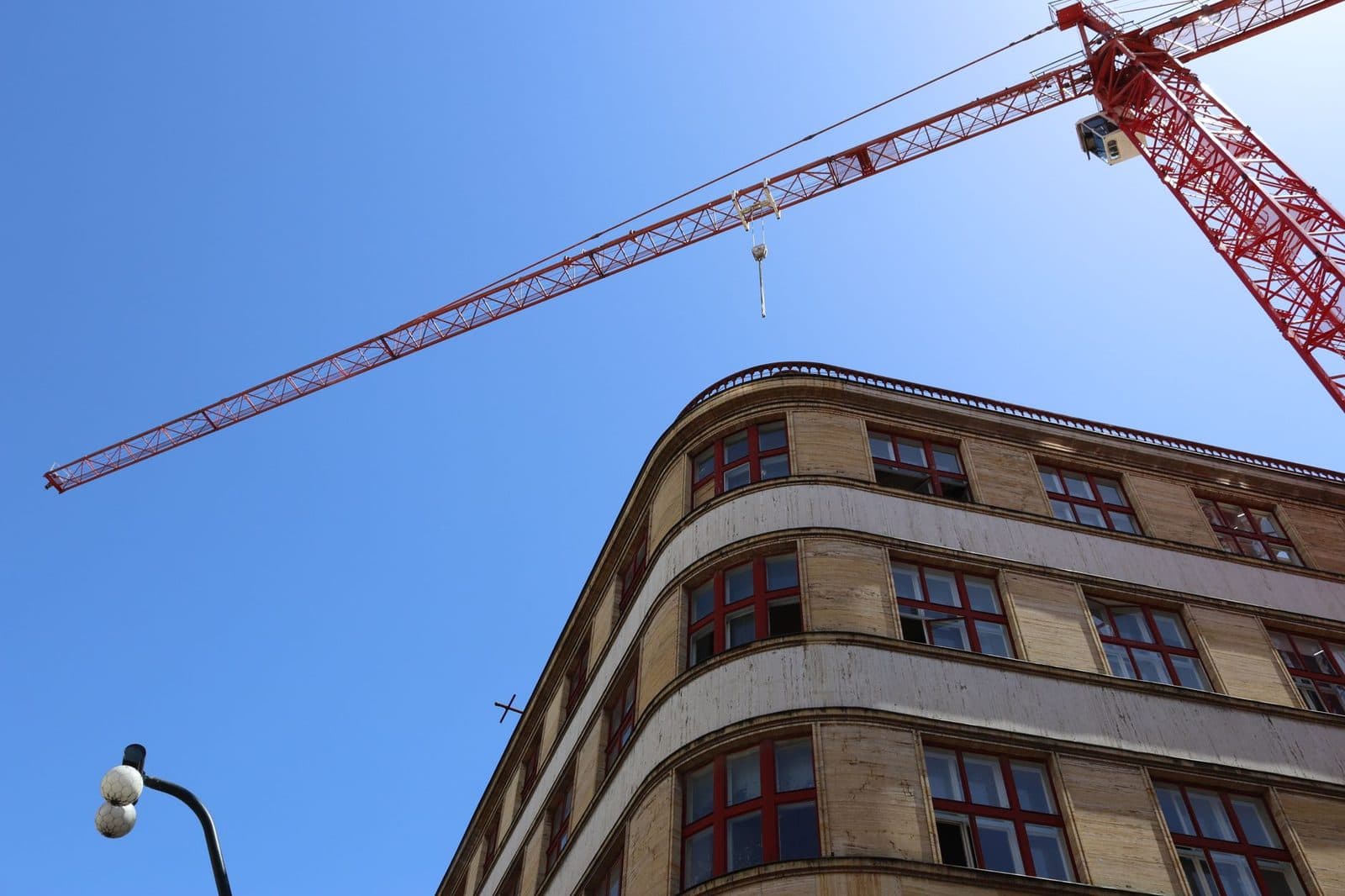 Grue de chantier rouge au-dessus d'un immeuble en travaux aux fenêtres à encadrements rouges, ciel bleu