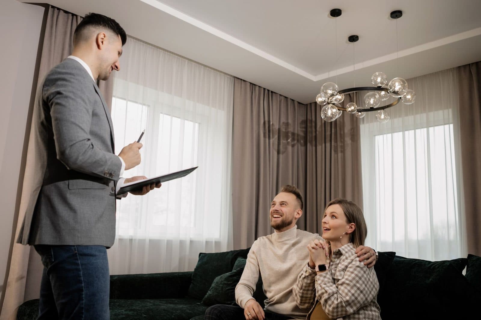 Un homme en costume avec un porte-documents présente un appartement à un couple assis sur un canapé