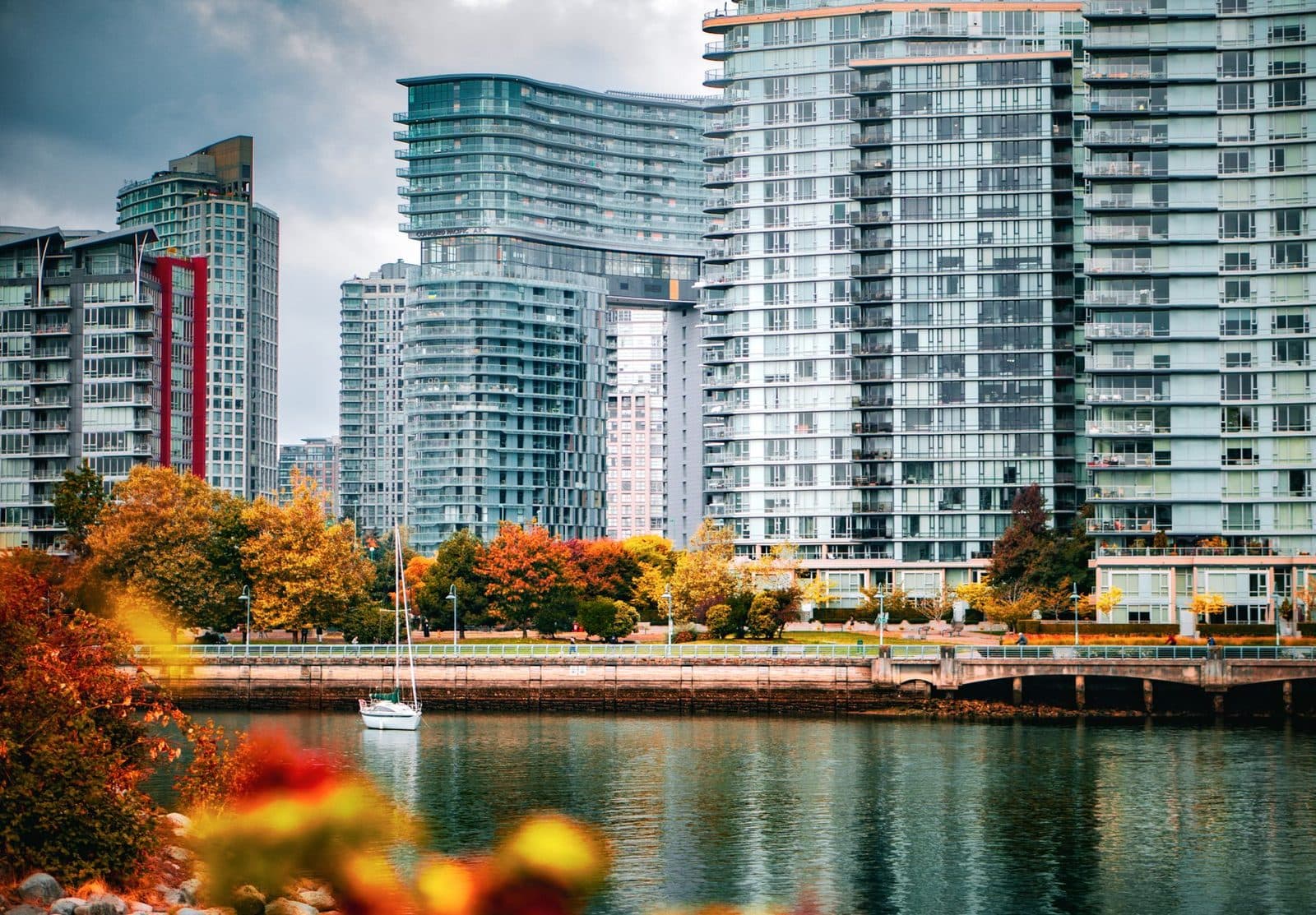 Immeubles résidentiels modernes avec balcons au bord de l'eau, arbres aux couleurs d'automne et voilier amarré