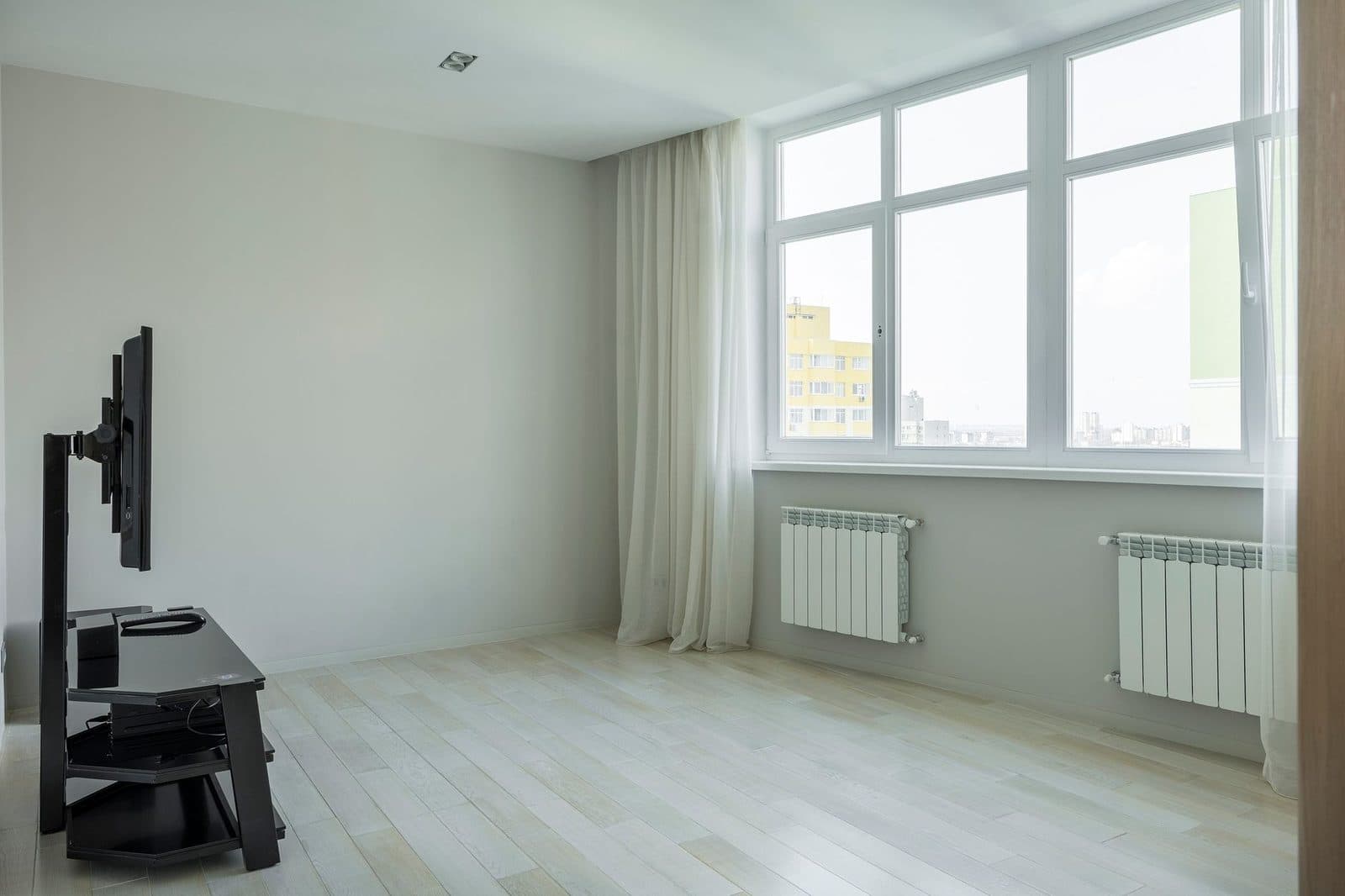 Pièce vide d'un appartement avec parquet clair, grandes fenêtres, rideaux et radiateurs blancs sous les fenêtres