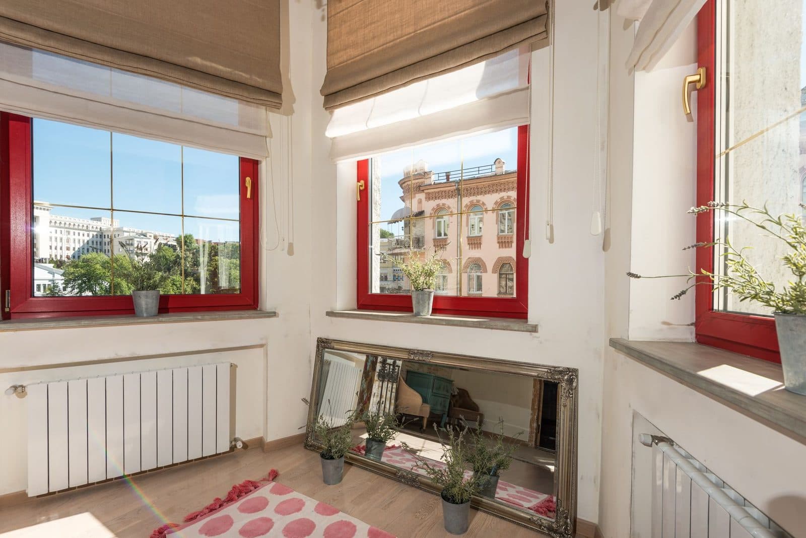 Pièce d'appartement ancien avec fenêtres à encadrement rouge, radiateurs blancs, miroir et plantes