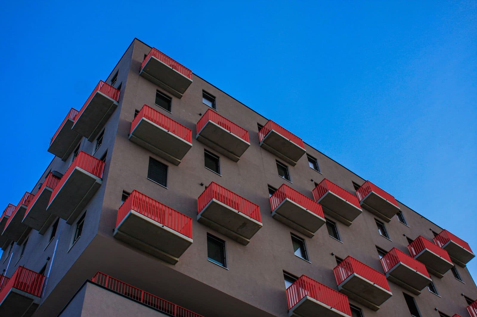 Façade d'un immeuble d'habitation en béton avec balcons à garde-corps rouges, vue en contre-plongée